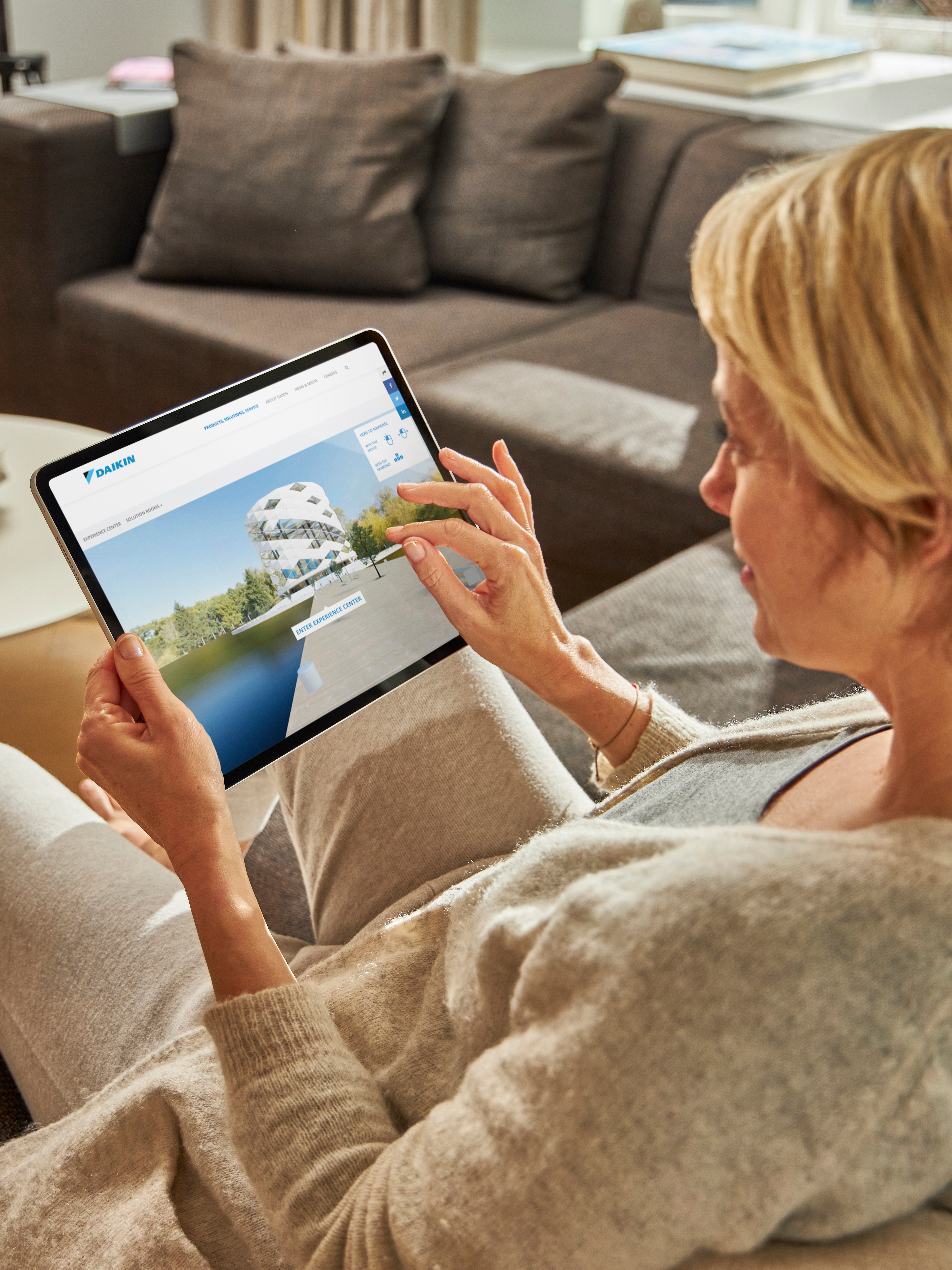 Egy nő a kanapén ülve nézi a klímákat tabletén, a virtuális élményközpontban